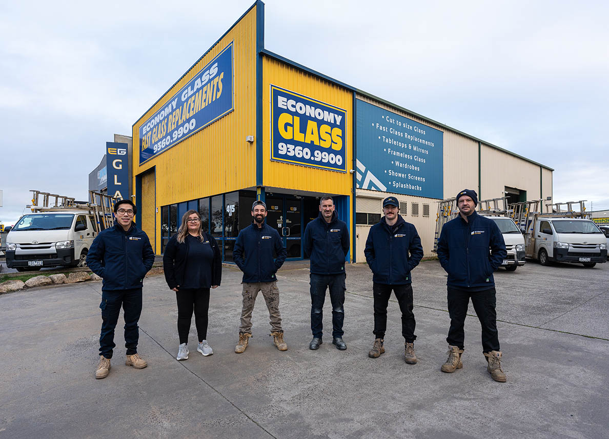 Six staff stand outside a yellow building with Economy Glass signs and vans