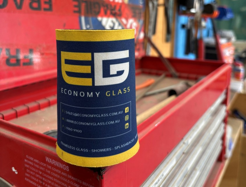 Navy blue stubby holder with Economy Glass logo sitting on a red toolbox