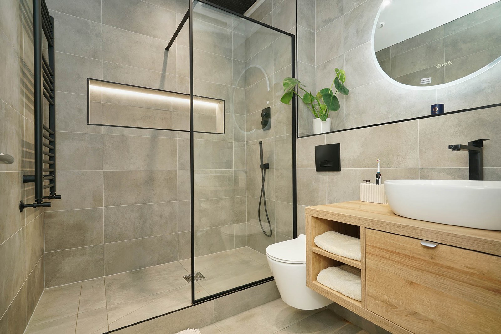 A walk-in shower with a black-framed glass panel, a tiled niche and a floor waste in a contemporary bathroom