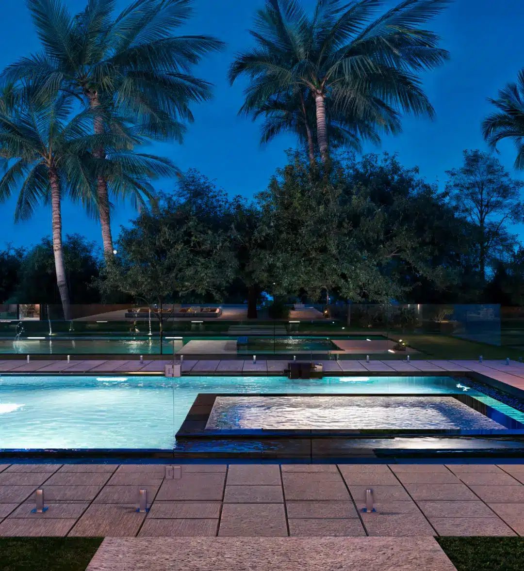 Frameless glass pool fencing on spigots around a lit swimming pool and spa at dusk